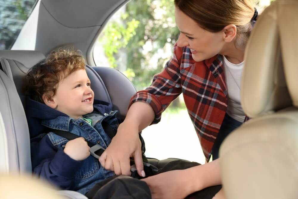 Mother fastening her son in child safety seat inside car.
