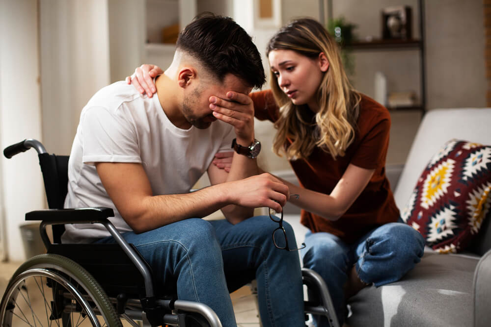 Wife comforting his sad husband on a wheelchair.