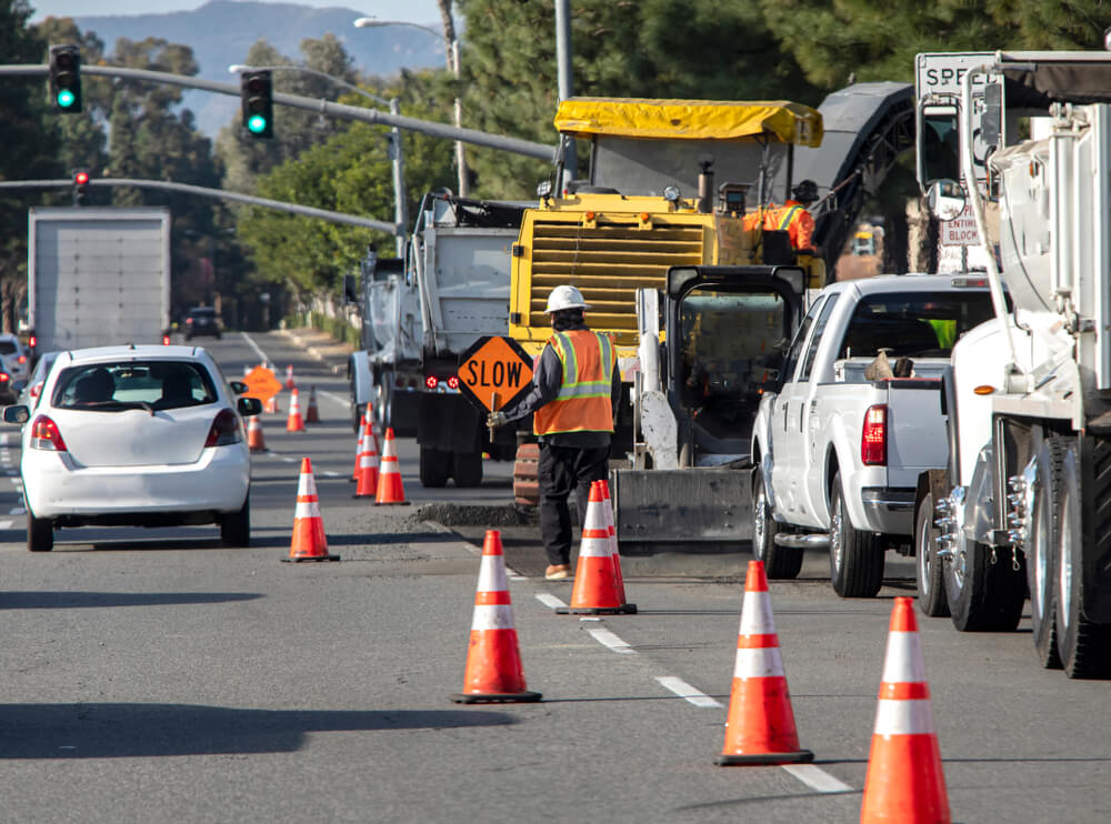 Construction worker putting sign on the road under repair.