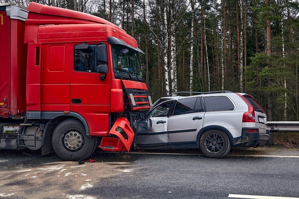 Red commercial truck vs sedan in highway collision.